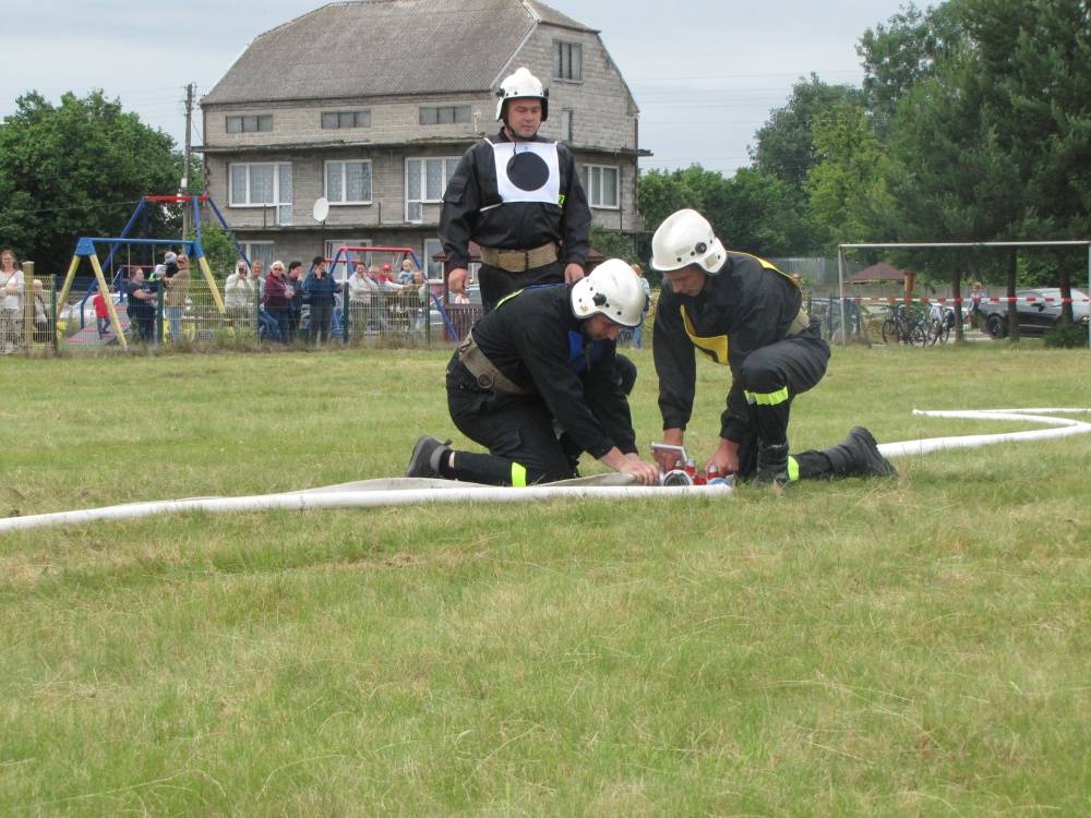 : Zawodnicy OSP Wola Mokrzeska łączący odcinki węża z rozdzielaczem podczas ćwiczenia bojowego.